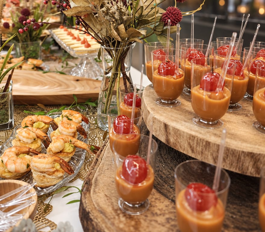 Coquetel com verrines e canapés de camarão servidos sobre base de madeira rústica.