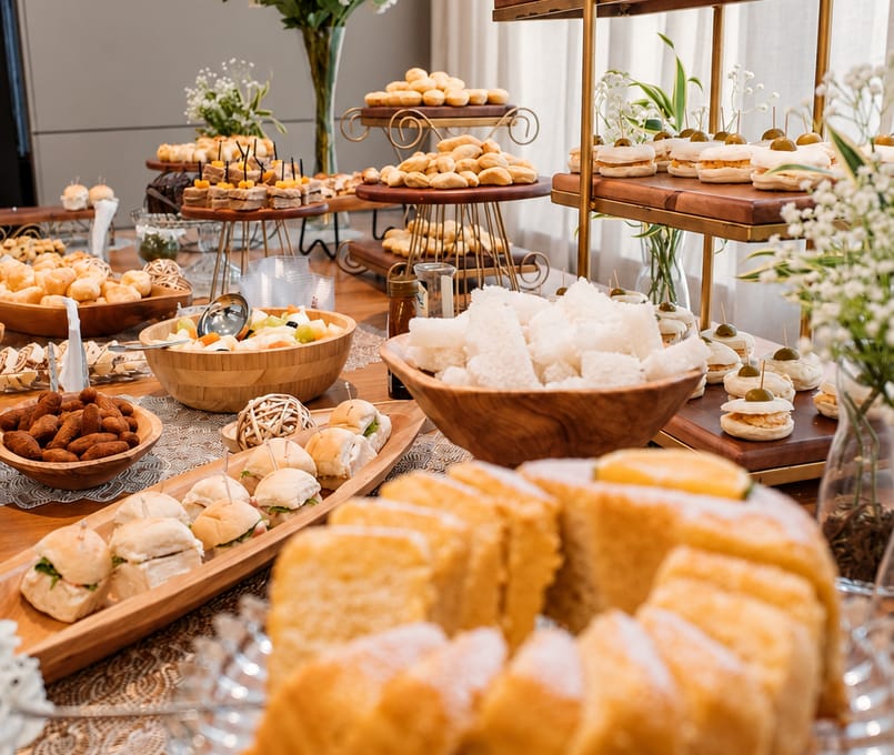 Travessas com mini sanduíches, castanhas e bolo fatiado sobre a mesa do evento.