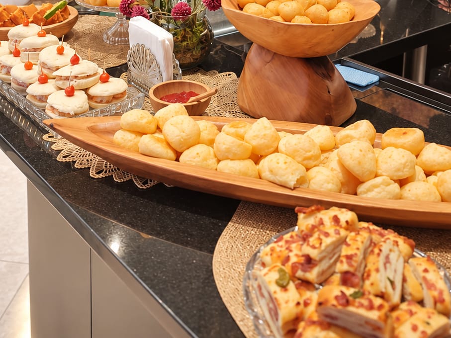 Bandeja de pães de queijo, docinhos e torta salgada em bancada de granito.